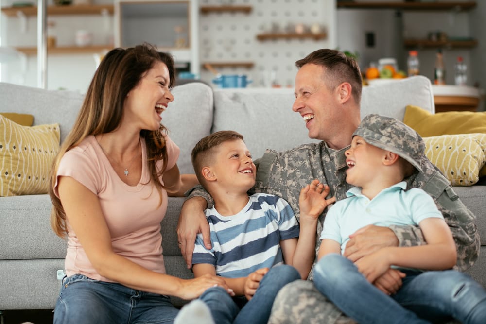 A smiling young girl hugs her mother from behind as they both sit together on a couch, sharing a joyful moment - Oro Valley Dentist A smiling young girl hugs her mother from behind as they both sit together on a couch, sharing a joyful moment - Oro Valley Dentist
