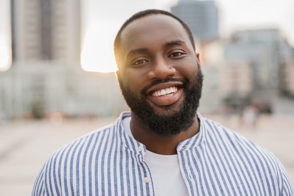 A man smiles warmly at the camera while standing outdoors, with a cityscape blurred in the background - Oro Valley Dentist A man smiles warmly at the camera while standing outdoors, with a cityscape blurred in the background - Oro Valley Dentist