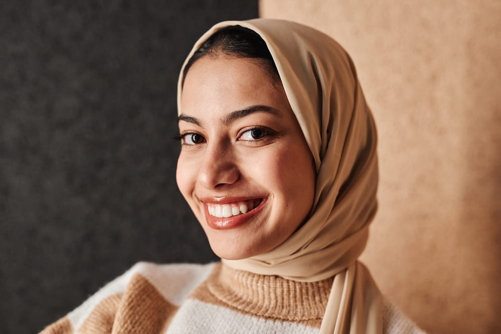 A woman wearing a beige hijab smiles warmly at the camera against a neutral background - Oro Valley Dentist A woman wearing a beige hijab smiles warmly at the camera against a neutral background - Oro Valley Dentist